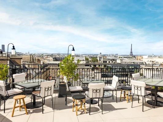 Terrasse du Montecito au Kimpton St Honoré Paris avec vue sur la tour Eiffel, tables en verre et chaises blanches, ciel bleu – cadre idéal pour les soirées Kimpton Club Live Music.
