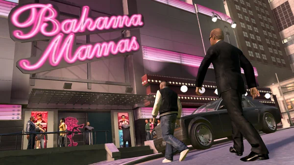 Capture d'écran de gameplay de Grand Theft Auto: The Ballad of Gay Tony montrant deux personnages masculins marchant devant la boîte de nuit Bahama Mamas à Liberty City la nuit.