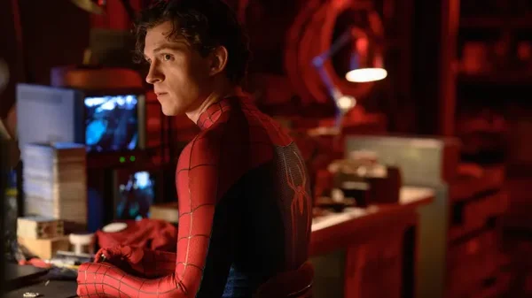 Scène du film Spider-Man: Brand New Day montrant un jeune homme en costume de Spider-Man assis à un bureau dans une pièce sombre remplie d'écrans et d'équipements, évoquant l'ambiance technologique du film.