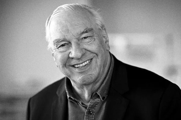 Portrait en noir et blanc de Didier Decoin, souriant, en veste sombre sur chemise à col