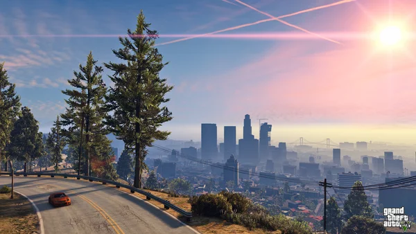 Capture d'écran de gameplay de Grand Theft Auto V montrant une vue panoramique sur la ville de Los Santos au coucher du soleil, avec une voiture de sport orange roulant sur une route sinueuse au premier plan.