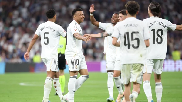 Joueurs du Real Madrid en maillot blanc célébrant sur la pelouse verte, avec Kylian Mbappé (numéro 10) et Jude Bellingham (numéro 5) visibles parmi l'équipe