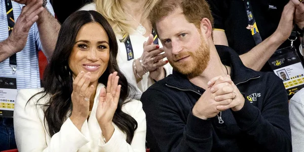 Le prince Harry et Meghan Markle assis dans une tribune de stade, applaudissant lors d'un événement public.