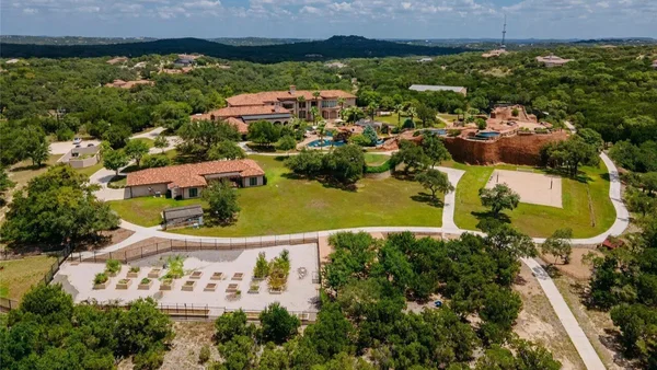 Vue aérienne du domaine de Tony Parker au Texas, avec une grande maison à toits en terre cuite, une piscine et des jardins paysagers entourés d'arbres verdoyants.