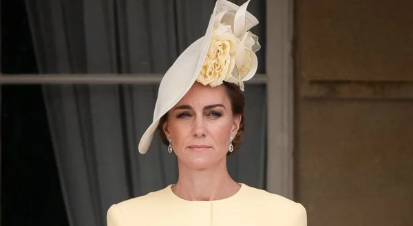 Kate Middleton en robe jaune pâle et chapeau fascinator assorti orné de fleurs en tissu, les cheveux relevés en chignon.