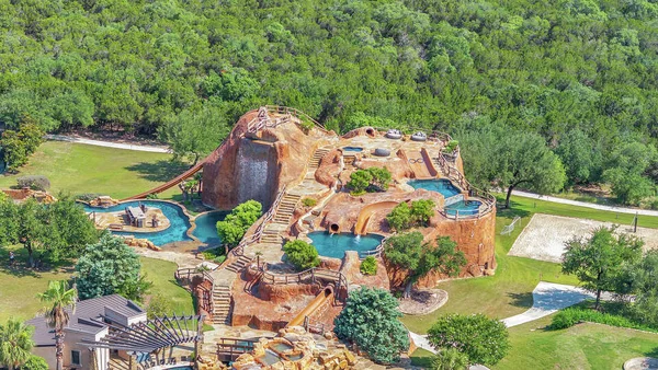 Vue aérienne du parc aquatique géant dans le jardin de la propriété de Tony Parker au Texas, avec des rochers artificiels, des piscines, des toboggans et une cascade.