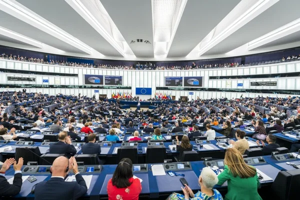 Vue d'ensemble de l'hémicycle du Parlement européen à Strasbourg, avec les députés européens applaudissant et le drapeau de l'UE en arrière-plan.