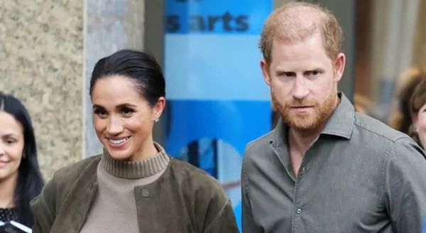 Le prince Harry et Meghan Markle marchant à l'extérieur, un panneau bleu visible en arrière-plan.
