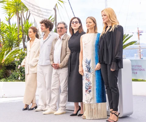 Groupe de six personnes, acteurs et réalisateurs, alignés pour un photocall en extérieur lors du Festival de Cannes 2025, avec des palmiers et un auvent blanc en arrière-plan.
