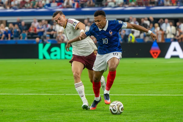 Kylian Mbappé en maillot bleu dribblant le ballon lors d'un match France-Espagne à la Coupe du Monde 2026, sous la pression d'un adversaire en blanc et marron.