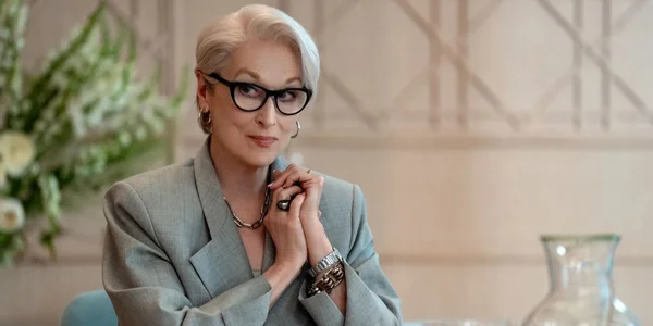 Meryl Streep incarne Miranda Priestly avec un carre platine et des lunettes noires, vetue d'un blazer gris, assise a une table, dans une scene evoquant Le Diable s'habille en Prada, en lien avec la vente aux encheres Christie's.