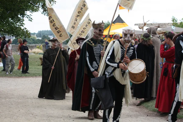 Procession médiévale à la Fête des Remparts de Dinan avec des participants en costumes d'époque, masques de squelette et bannières à inscriptions runiques, ambiance de reconstitution historique.