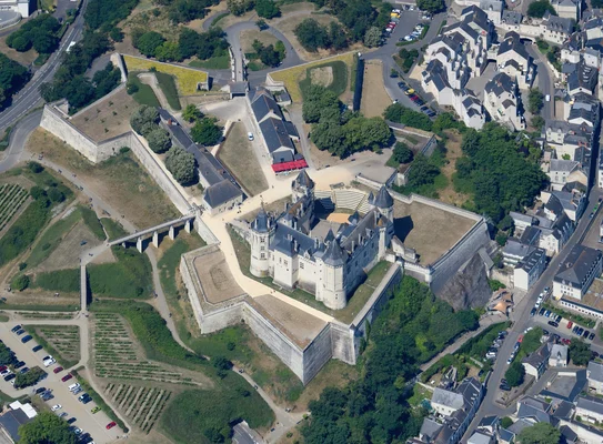 Vue aérienne du Château de Langeais, forteresse médiévale en France, montrant son donjon en pierre, ses remparts et les vignobles adjacents, en arrière-plan de la Loire.