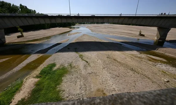 Pont en pierre enjambant le lit de la Loire fortement réduit en été, avec des bancs de sable et de graviers exposés et de minces filets d'eau sinueux, illustrant un étiage saisonnier normal.