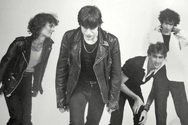 Photographie en noir et blanc du groupe Téléphone, composé de quatre membres habillés en style punk avec blousons de cuir et vêtements sombres, devant un fond neutre.