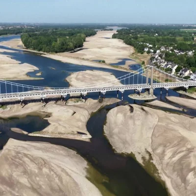 Vue aérienne d'un pont suspendu enjambant la Loire à très bas niveau d'eau, révélant d'immenses bancs de sable et des îles exondées, illustrant un étiage saisonnier typique du fleuve.