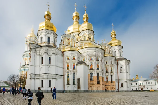 Monastère Saint-Michel au dôme doré à Kiev, avec ses murs blancs et ses coupoles dorées sous un ciel bleu, des touristes traversant la cour pavée au premier plan.