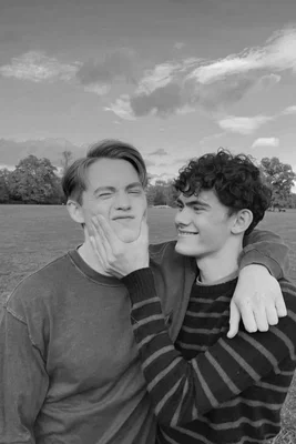 Photographie en noir et blanc de Joe Locke et Kit Connor dans un parc, Kit Connor tenant tendrement le visage de Joe Locke en souriant, illustrant l'intimité de leur relation dans Heartstopper Forever.