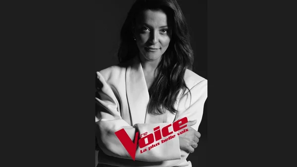 Portrait en noir et blanc de Camille Lellouche, les bras croisés, vêtue d'un blazer blanc, avec le logo rouge de The Voice superposé sur l'image.