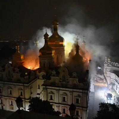 Incendie nocturne de la cathédrale de la Dormition de Kiev, ses dômes dorés et son toit en flammes, une épaisse fumée s'élevant dans le ciel, avec des pompiers au sol à droite utilisant une échelle pour combattre le feu.
