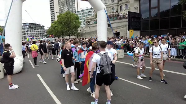 Le casting de la série Heartstopper défilant lors de la Pride de Londres en 2022, sous des arches gonflables blanches, entouré de spectateurs et de barrières de sécurité.