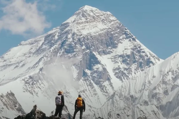 Deux alpinistes avec sacs à dos sur une crête rocheuse, contemplant un sommet enneigé, évoquant l'ascension de l'Everest par Inoxtag et Mike Horn.