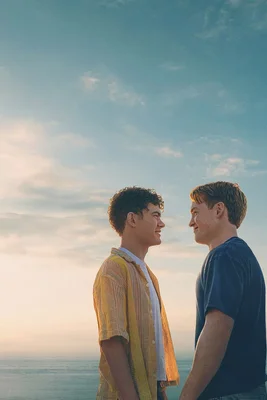 Joe Locke et Kit Connor dans le film Heartstopper Forever, face à face sur une plage au coucher du soleil, portant respectivement une chemise jaune et un t-shirt bleu marine.