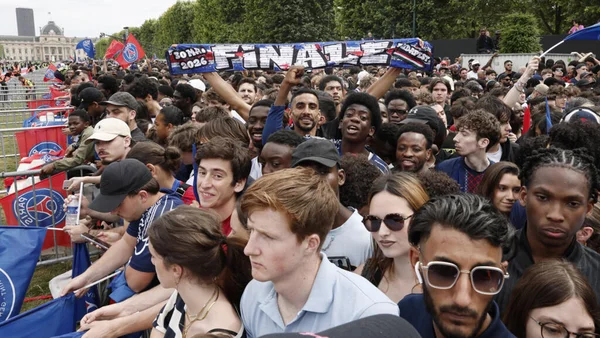 Une foule de supporters du PSG rassemblée en extérieur, brandissant des drapeaux du club et une écharpe géante 'FINALE 2026' lors d'un rassemblement de fans à Paris.