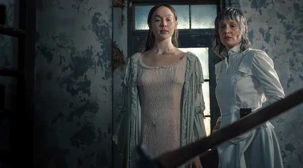 Ella Beatty et une autre actrice dans une pièce sombre et délabrée aux murs écaillés, l'une en nuisette et robe de chambre, l'autre en chemisier et jupe d'époque, dans l'ambiance du teaser de Monster: The Lizzie Borden Story