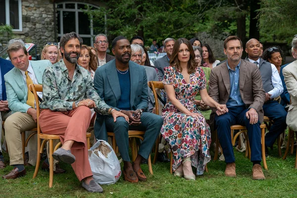 Steve Carell et Rose Byrne assis sur des chaises en bois sur une pelouse, lors d'un événement en extérieur, vêtus de tenues semi-formelles
