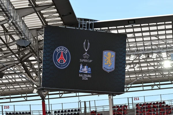 Écran LED géant du stade de Salzbourg affichant les logos du PSG et d'Aston Villa avec le trophée de l'UEFA Super Cup et la mention 'Salzburg 2026', sous la charpente métallique du toit.