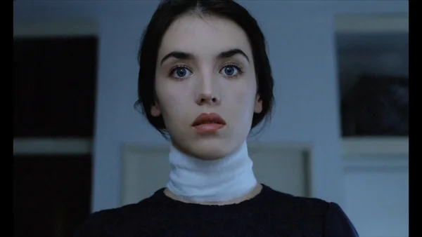 Isabelle Adjani dans le film Possession d'Andrzej Zulawski, portant une minerve blanche et un haut noir, regardant la caméra avec une expression neutre