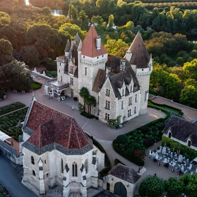 Vue aérienne du château des Milandes en Dordogne, demeure historique de Joséphine Baker, avec ses tours coniques, sa chapelle et ses jardins soignés baignés de lumière chaude