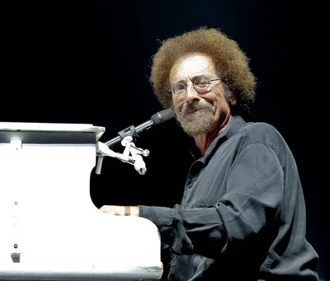 Jean Schultheis, directeur musical de STARS 80 & FRIENDS, jouant du piano blanc sur scène, avec son afro, sa barbe et ses lunettes, lors d'une représentation au Zénith d'Orléans.