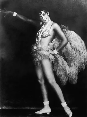 Joséphine Baker en costume de scène des années 1920, parée de perles et de plumes, dans une pose dynamique lors de la Revue Nègre.