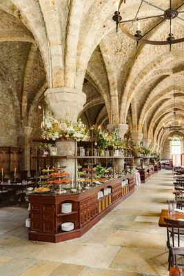 Grande salle voûtée de l'abbaye des Vaux-de-Cernay avec plafonds gothiques à nervures, buffet élégant avec compositions florales et lustres en fer forgé pour un événement de luxe