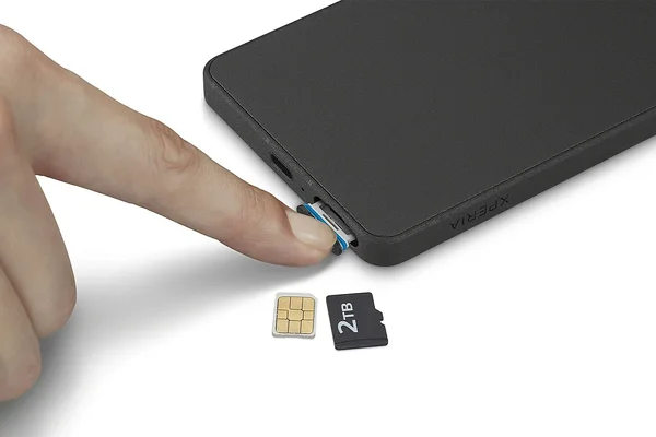 Gros plan d'une main insérant un tiroir SIM dans le côté d'un smartphone Sony Xperia noir, avec une carte SIM et une carte microSD de 2 To posées sur une surface blanche en dessous