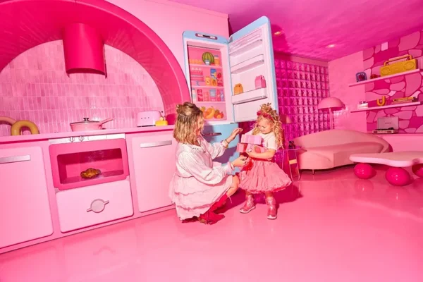 Une femme et une fillette dans une pièce entièrement rose de l'exposition Barbie The Dream Experience, avec un canapé en forme de rein et une cuisine stylisée, évoquant l'univers de la poupée Barbie à Paris