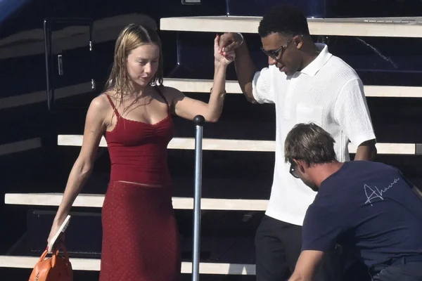 Ester Expósito en robe rouge aux cheveux mouillés tenant la main de Kylian Mbappé en polo blanc et lunettes de soleil sur un yacht lors de leurs vacances en Sardaigne