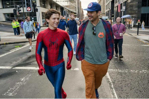 Tom Holland en costume de Spider-Man et le réalisateur Destin Daniel Cretton marchant côte à côte sur un plateau de tournage urbain, le réalisateur portant une casquette de baseball et une chemise à carreaux.