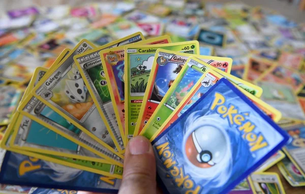 Main étalant des cartes Pokémon en français, dont Galegon et Carabini, sur un fond flou de cartes dispersées, illustrant le butin estimé à plus de 80 000 euros lors du cambriolage d'une boutique en Maine-et-Loire.