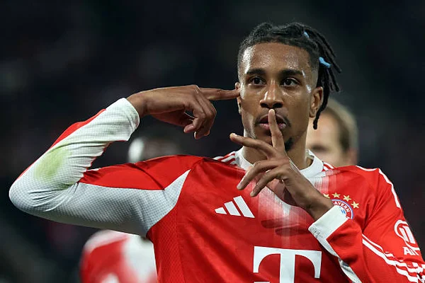 Michael Olise, milieu de terrain français du Bayern Munich, célébrant après avoir marqué un but en Ligue des champions, doigt sur la tempe et l'autre sur les lèvres.