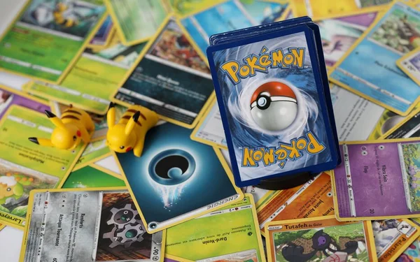 Photographie en plongée rapprochée montrant une collection de cartes Pokémon éparpillées, avec un deck box bleu au logo Poké Ball et deux figurines Pikachu jaunes, illustrant le butin du braquage de la boutique Pokémon à 80 000 euros en Isère.