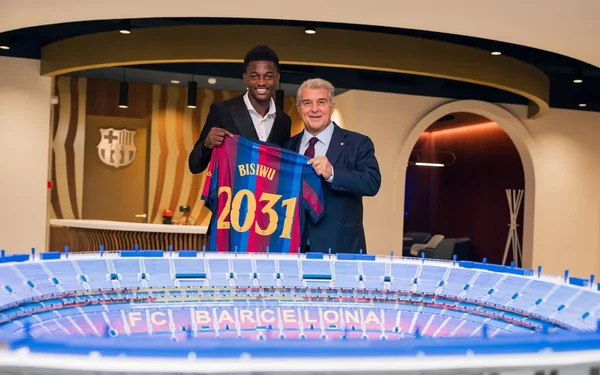 Jesse Bisiwu, 18 ans, présenté comme nouveau joueur du FC Barcelone : le prodige camerounais pose avec un dirigeant en costume, tenant le maillot blaugrana à son nom et le numéro 2031, devant une maquette du stade.