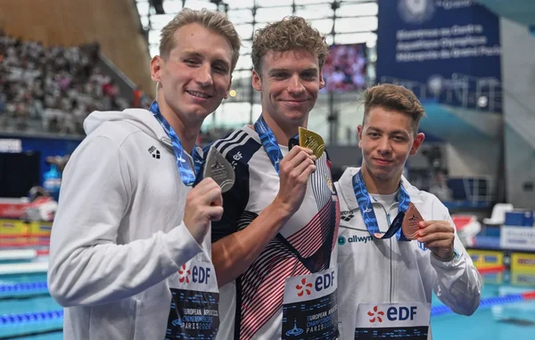 Léon Marchand célébrant sa victoire en or aux Championnats d'Europe de natation, aux côtés de Mary-Ambre Moluh, sous les projecteurs de la piscine.