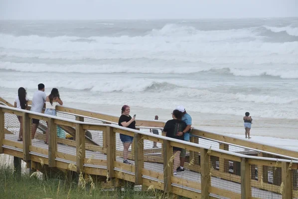 Plage fermée et sacs de sable empilés sur la côte du Golfe alors que la tempête tropicale Bertha approche, avec un ciel menaçant et des vagues agitées.