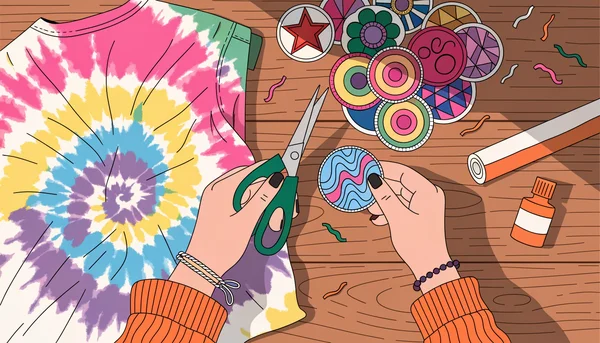 Composition à plat, vue de dessus, montrant des mains organisant du matériel d'upcycling sur une table en bois : un t-shirt tie-dye à motif spirale coloré, des patchs thermocollants variés, des ciseaux à tissu, un rouleau de ruban ourlet thermocollant et une petite bouteille de peinture textile.
