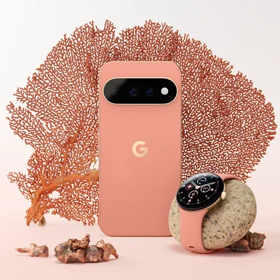 Smartphone Google Pixel 11 en couleur corail et montre Google Pixel Watch assortie, disposés sur une surface rose avec du corail rouge et des pierres.