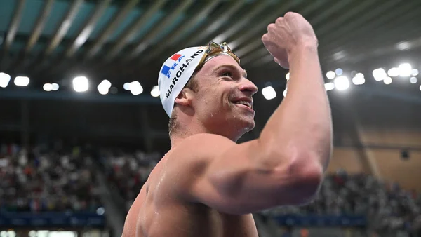 Un nageur néerlandais portant une casquette blanche avec 'HOLLAND' lève le poing en signe de victoire dans un bassin de natation intérieur lors des Championnats d'Europe.