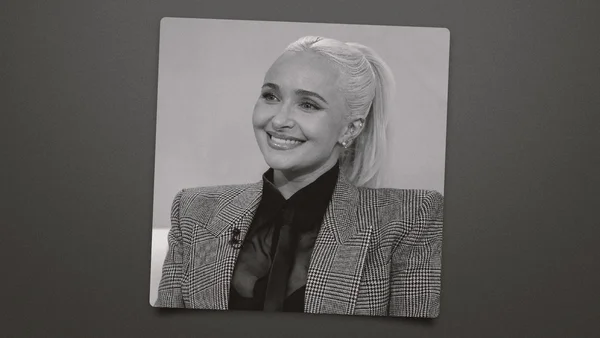 Hayden Panettiere, actrice de Heroes, en photo noir et blanc, souriante, les cheveux blonds attachés en queue-de-cheval, portant un blazer à carreaux sur une chemise sombre avec un nœud.